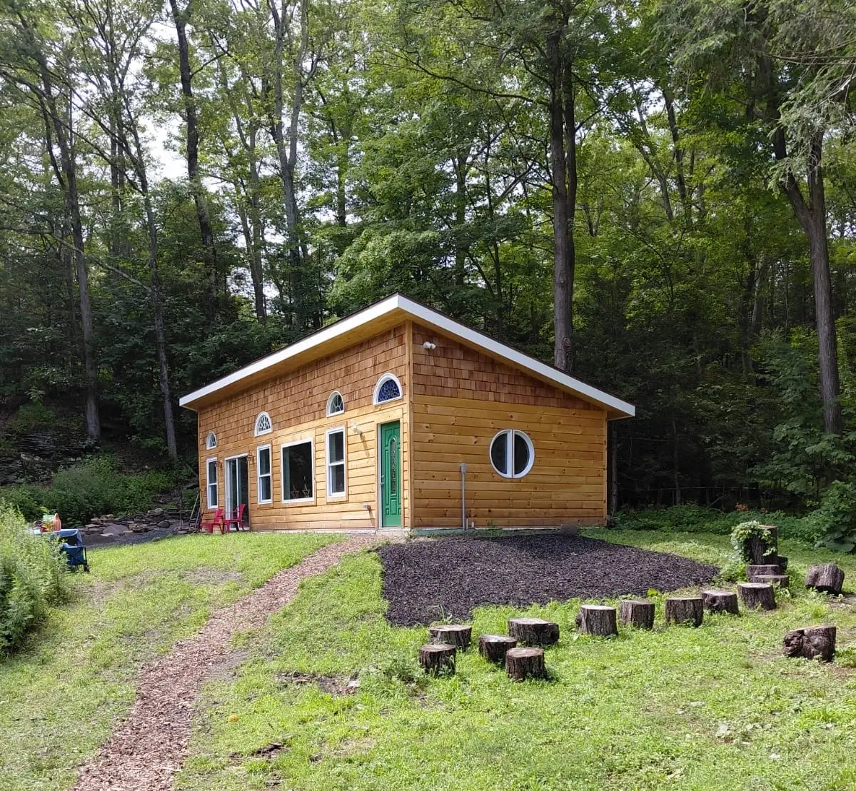Cedar-shingled StarryPines Studio with green door set among the trees in summer