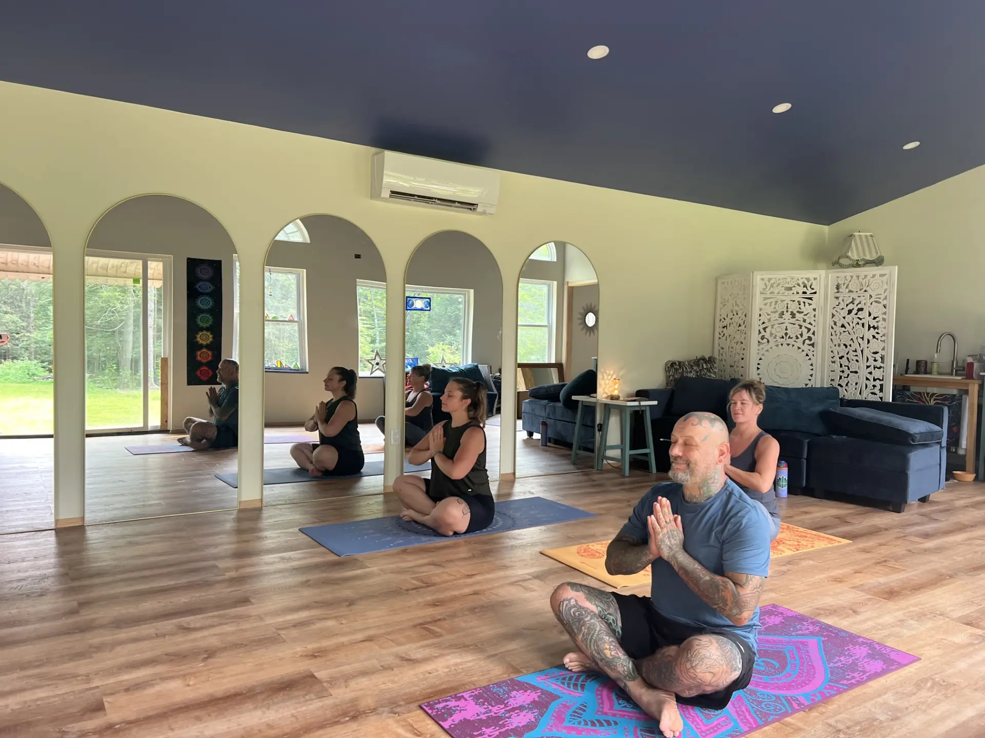 Group meditating on yoga mats in front of the studio's arched mirrors
